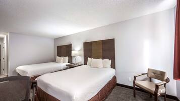 A hotel room with two beds, a desk, a chair, and a lamp.
