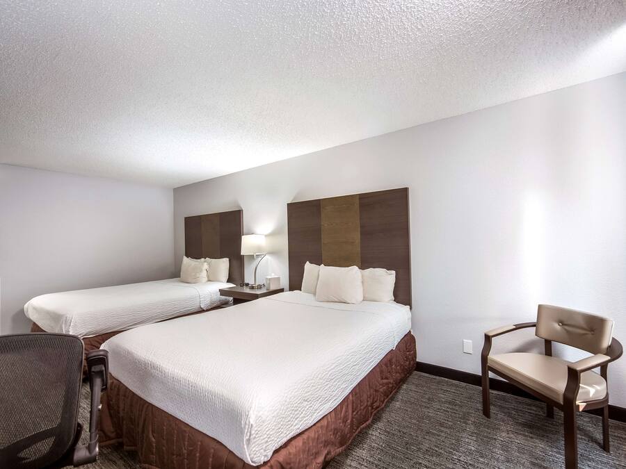 A hotel room with two beds, a desk, a chair, and a lamp.