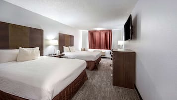 Ein Hotelzimmer mit zwei Betten, einem Flachbildfernseher, einem Schreibtisch und einem Fenster mit Vorhängen.