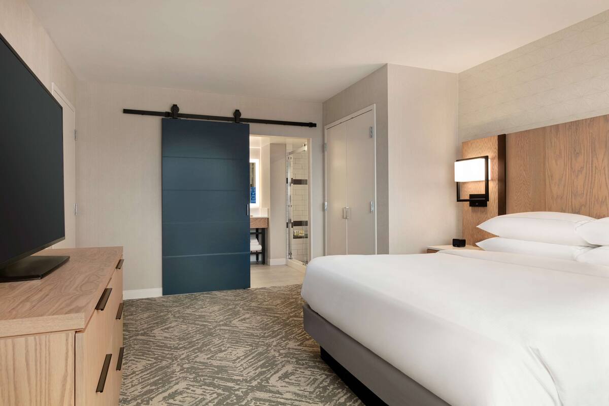A hotel room with a bed, a TV on a wooden dresser, a blue sliding door, and a nightstand with a lamp.