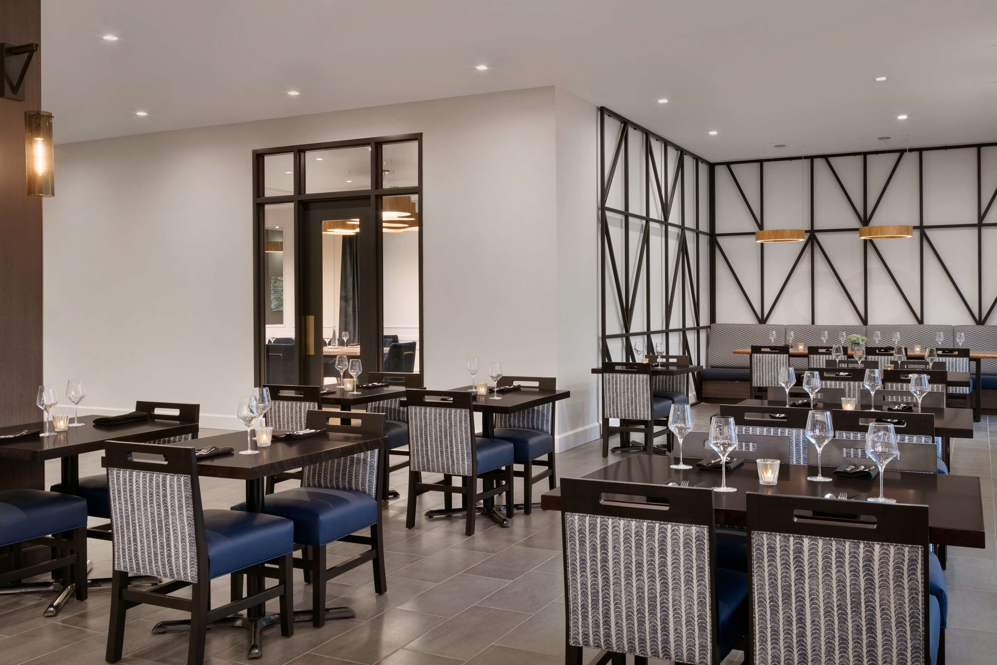 A modern dining area with multiple tables and chairs, a large mirror, and a geometric wall design.