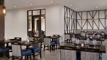 A modern dining area with multiple tables and chairs, a large mirror, and a geometric wall design.