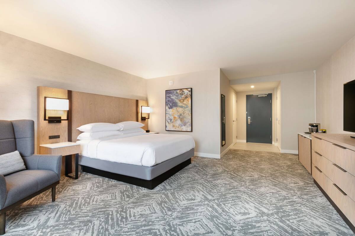A hotel room with a bed, a desk, a chair, a dresser, and a painting on the wall.