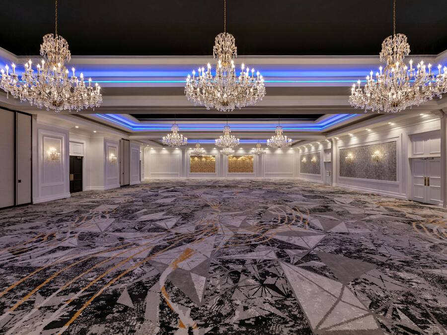 A spacious hall with multiple chandeliers, white walls, and a patterned carpet.