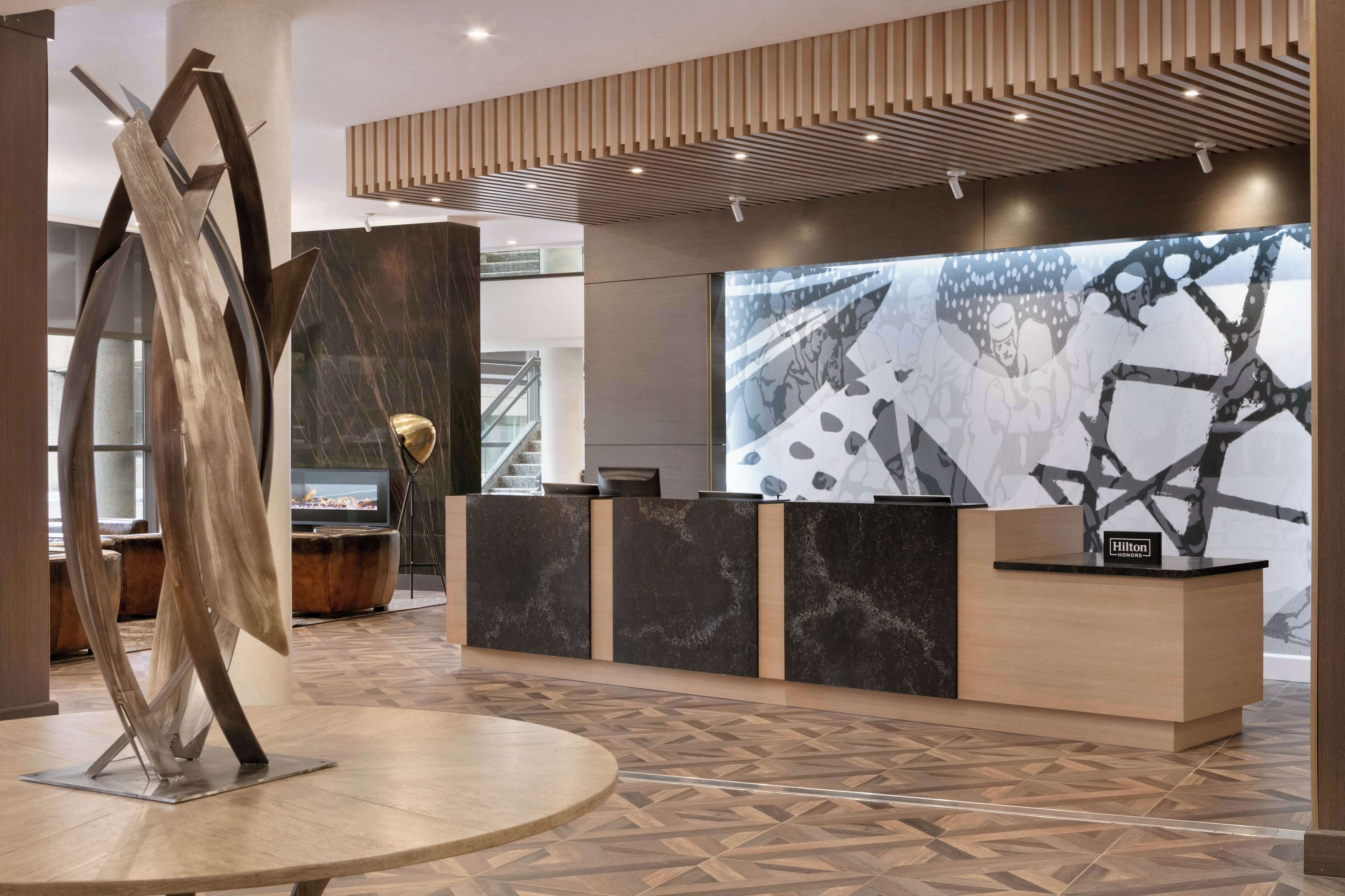 A modern reception area with a wooden reception desk, a large abstract artwork on the wall, and a unique metal sculpture.
