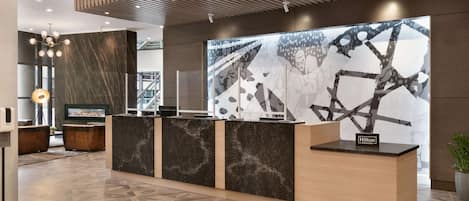 A modern hotel reception area with a reception desk, a large abstract wall art, and a geometric patterned floor.