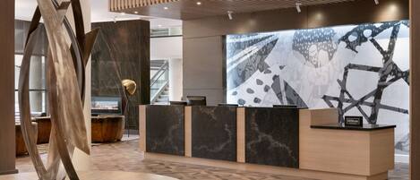 A modern hotel reception area with a wooden reception desk, a large abstract painting, and a unique metal sculpture.