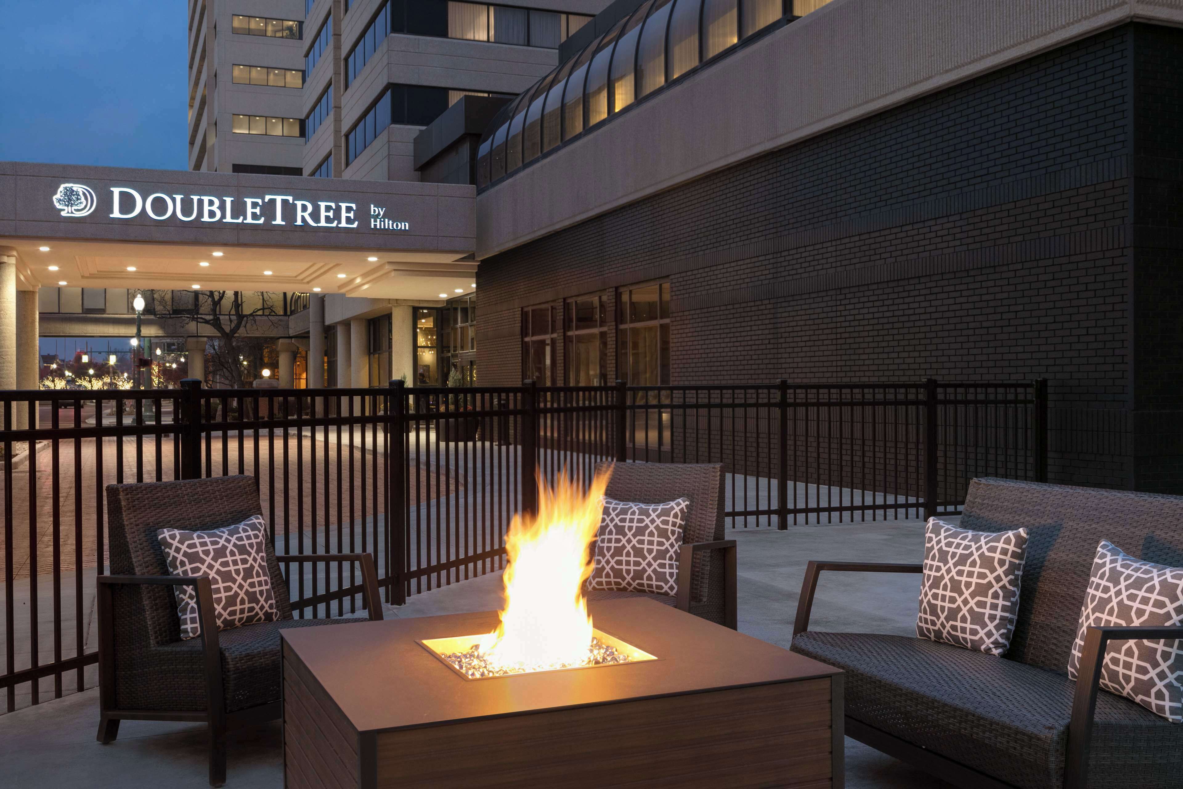 Un área de estar al aire libre con una chimenea, un letrero de DoubleTree by Hilton y fachada de edificio de ladrillo.