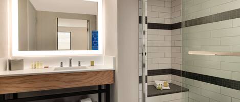 Un bagno moderno con un ampio specchio, un mobile vanitario in legno, box doccia in vetro e asciugamani ordinatamente piegati.