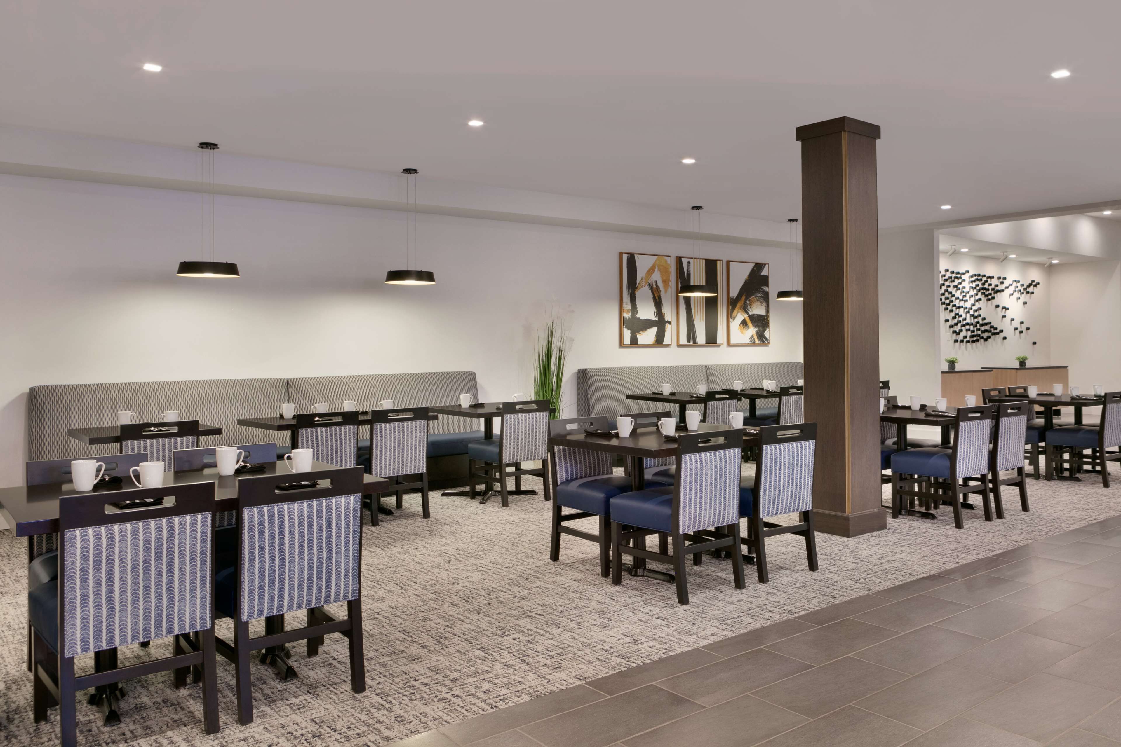 A modern hotel dining area with tables and chairs, a reception desk, and artwork on the walls.
