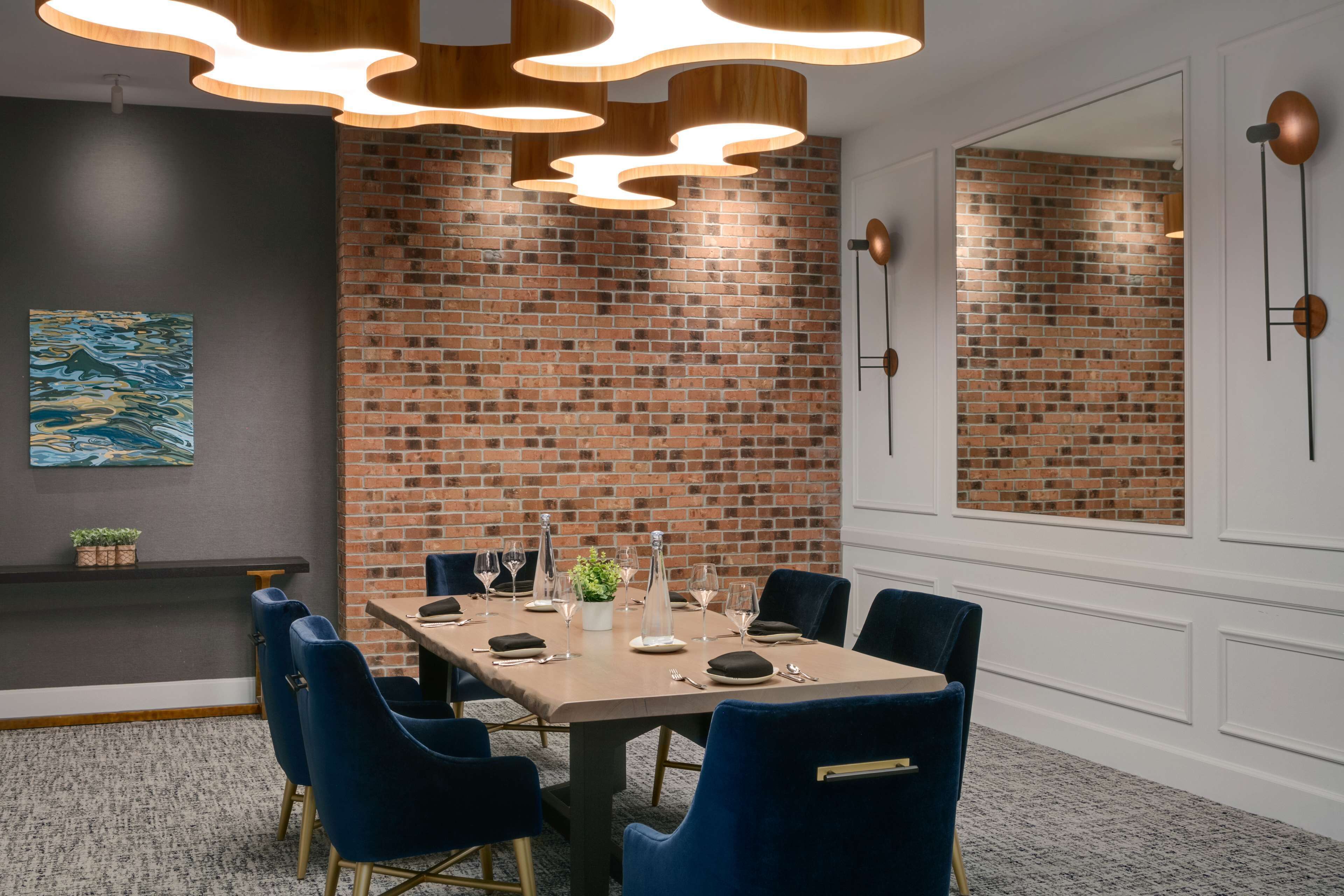 Ein Konferenzraum mit Backsteinwand, einem langen Tisch mit Stühlen und moderner Pendelleuchte.