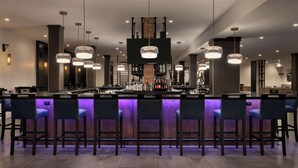 Zona de bar moderna con una barra central, taburetes, iluminación colgante y una pared de ladrillo decorativa.