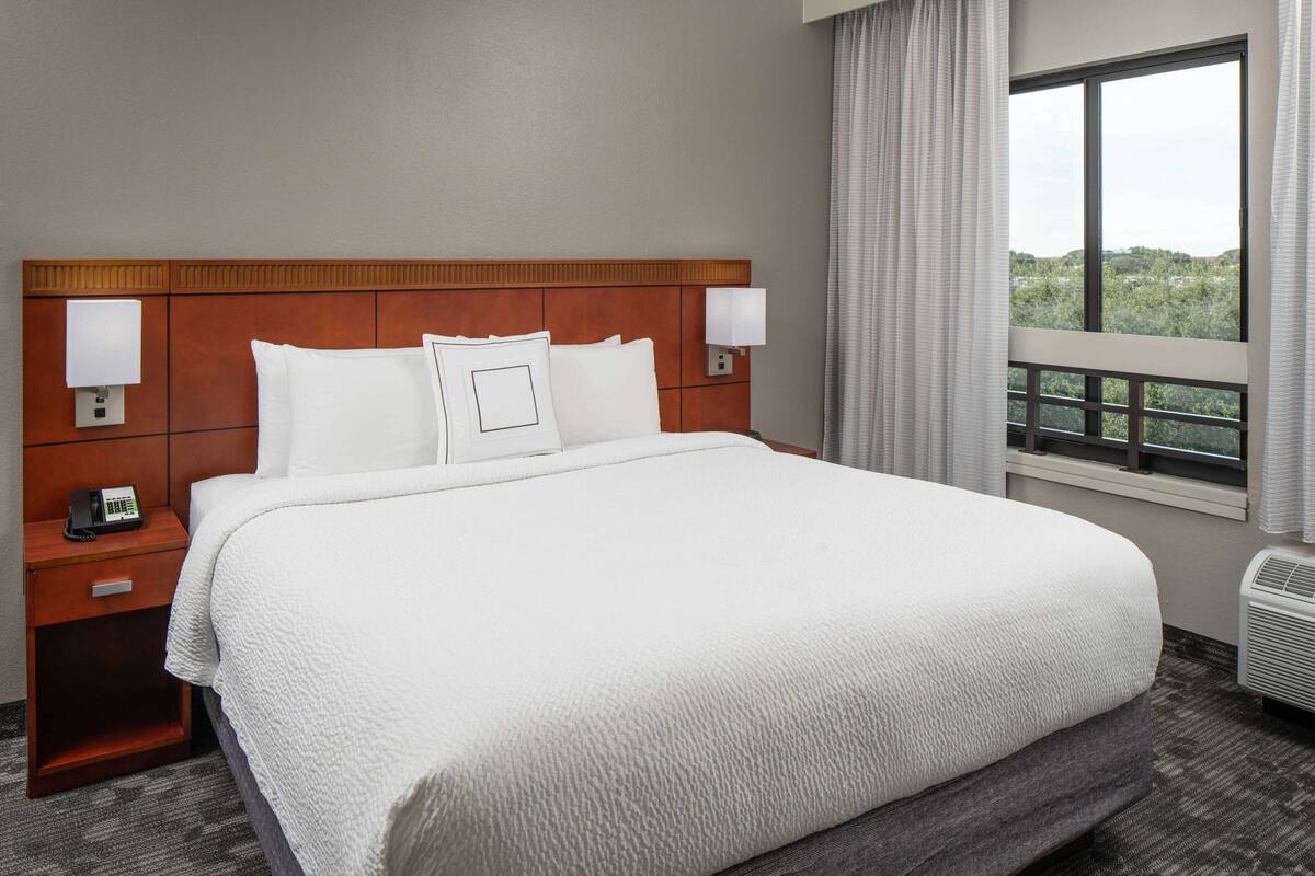 A hotel room with a large bed, two bedside tables, a telephone, and a window with curtains.