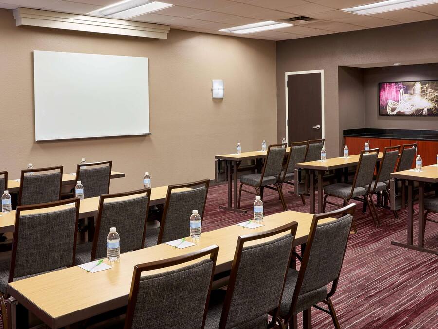 Un salón de conferencias con varias mesas y sillas, una pizarra y una pantalla de proyección.