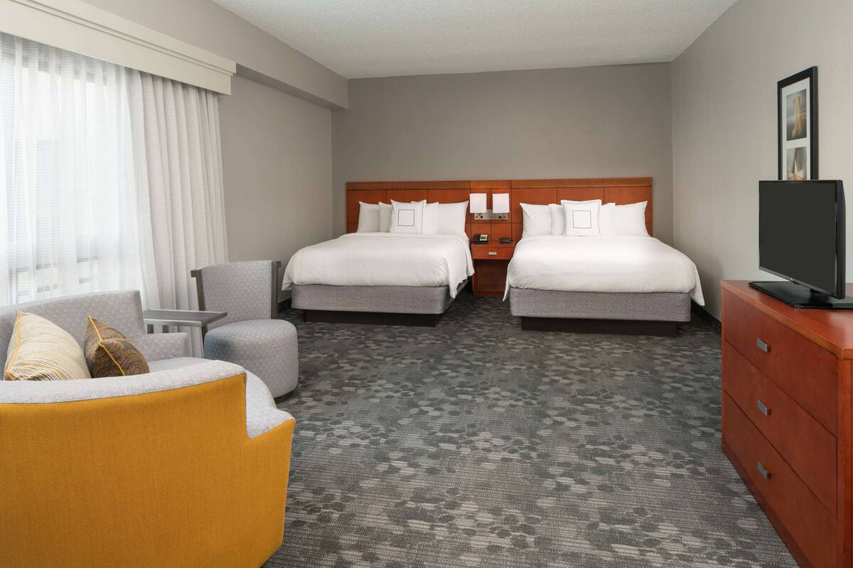 A hotel room with two beds, a sofa, a TV, and a desk.