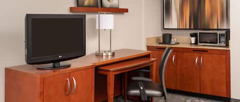 A hotel room with a wooden desk, an LG flat-screen TV, a modern lamp, a microwave, and a large abstract painting on the wall.