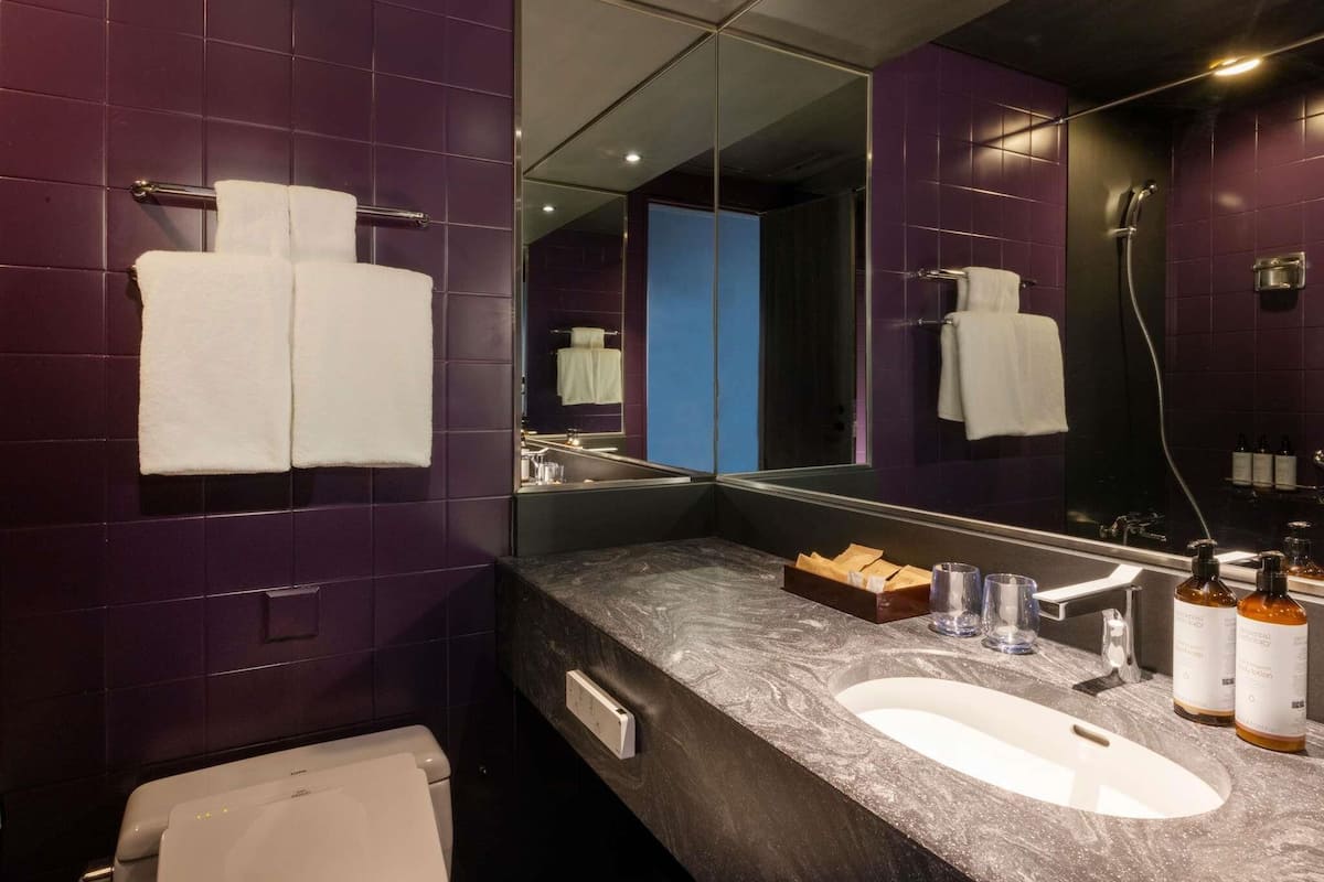 Un baño moderno con azulejos morados, un espejo grande, un lavabo blanco y una ducha.