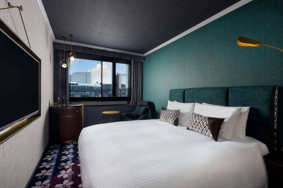 A hotel room with a large bed, a desk, a chair, and a view of the city.