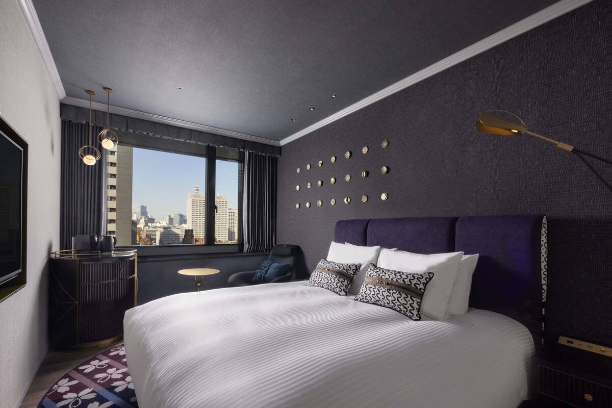 A modern hotel room with a large bed, a city view, a vanity with a mirror, and a unique wall decoration.