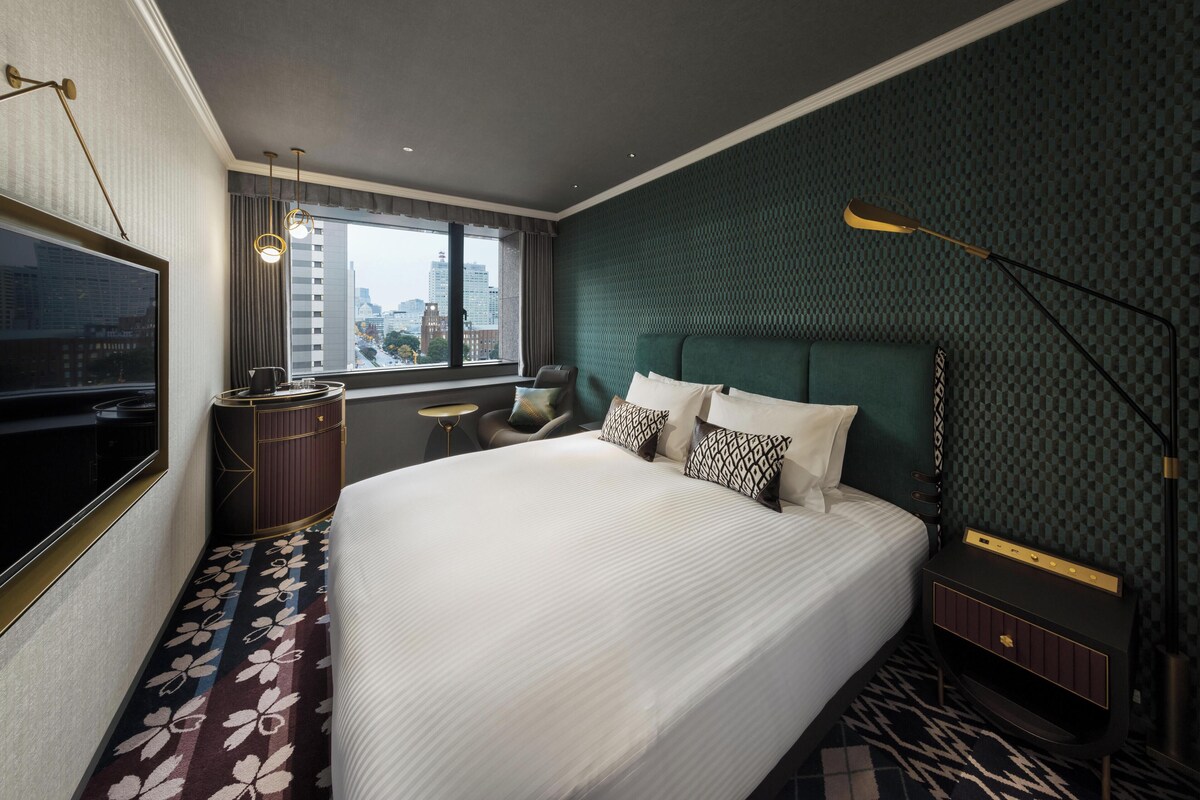 A hotel room with a large bed, a TV, a desk, and a view of the city.