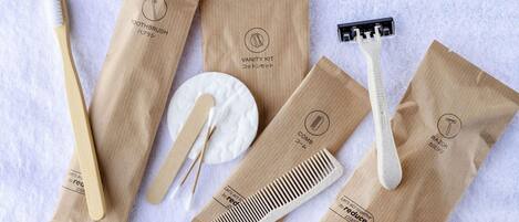 A set of personal care items including a toothbrush, razor, comb, and cotton swab, all packaged in brown paper bags with eco-friendly messages.
