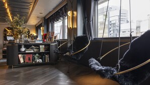 A modern interior with a black leather sofa, a bookshelf, and a city view through large windows. - Mercure Tokyo Hibiya (Tokyo)