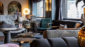 A modern lounge area with seating, a coffee table, a bookshelf, and a large window with a view of buildings. - Mercure Tokyo Hibiya (Tokyo)