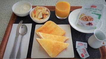 Bandeja de desayuno con tostadas, fruta, jugo, yogur, cereales y un sobre de kétchup Heinz.