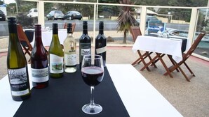 A table with wine bottles and a glass of red wine, set outdoors with a view of parked cars and a building in the background. - Best Western Burnie Murchison Lodge (Somerset)