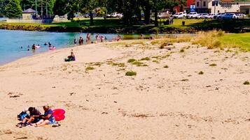 Ein Strand mit badenden und entspannenden Menschen, im Hintergrund ein Gebäude mit der Aufschrift 'Murchison Lodge' und ein Rasenbereich mit Bäumen.