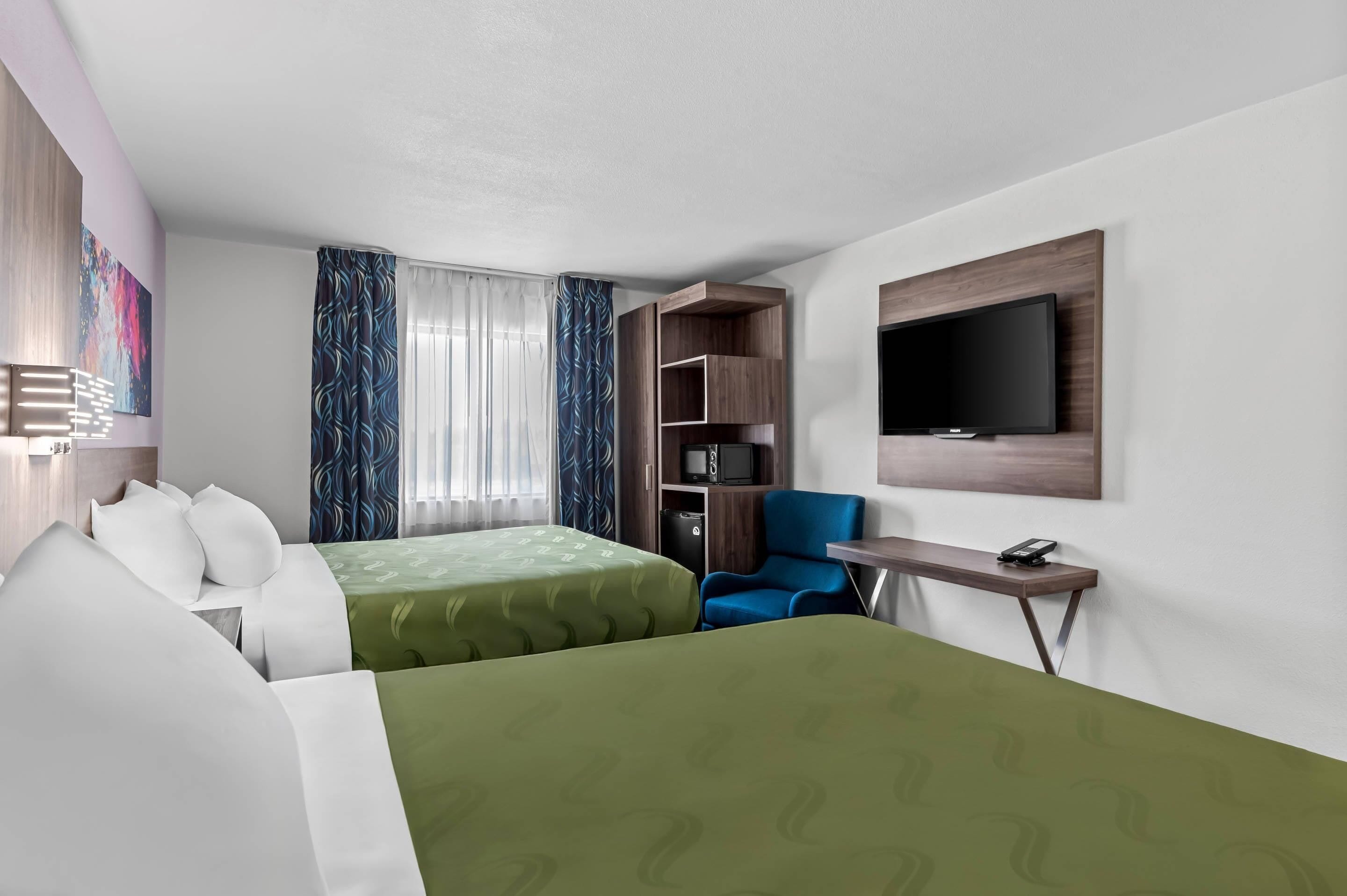 A hotel room with two beds, a TV, a desk, and a chair.