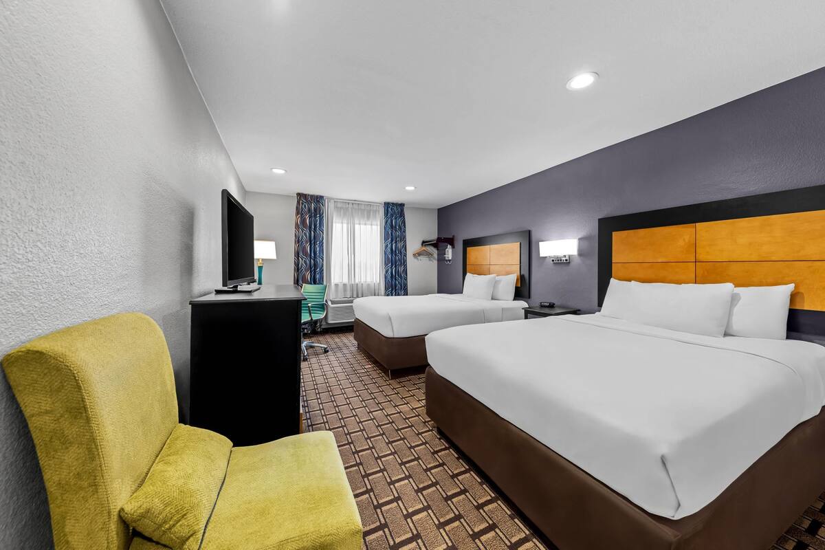 A hotel room with two beds, a desk, a chair, and a television.