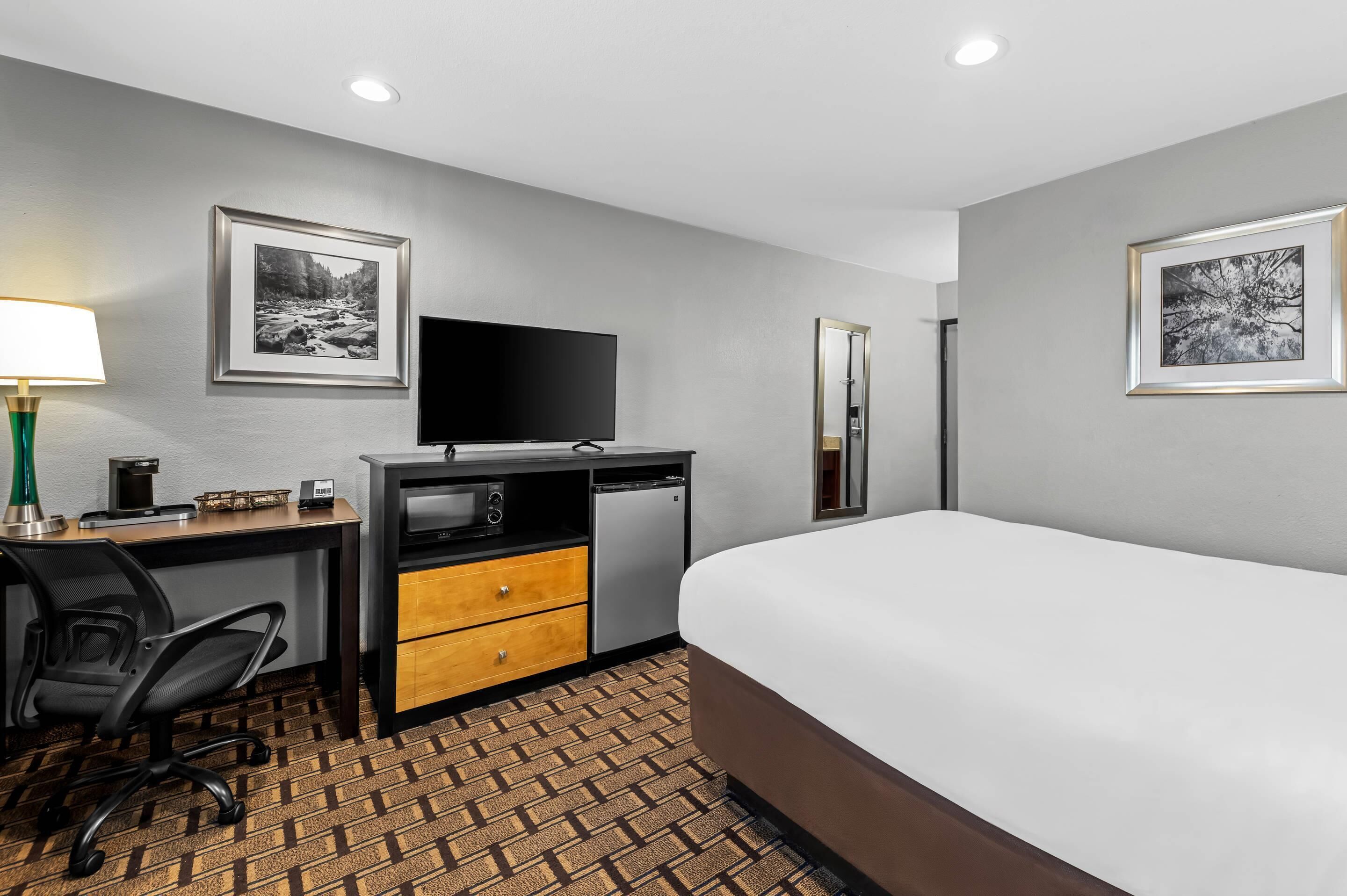 Ein Hotelzimmer mit Bett, Schreibtisch, Stuhl, Fernseher und zwei gerahmten Bildern an der Wand.