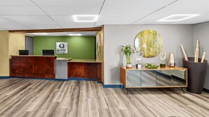 A reception area with a wooden reception desk, a green wall, and a large mirror with a circular decorative piece.