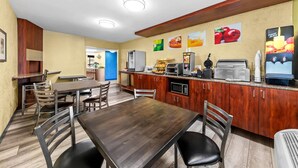 A restaurant with wooden tables and chairs, a counter with food items, and a refrigerator.
