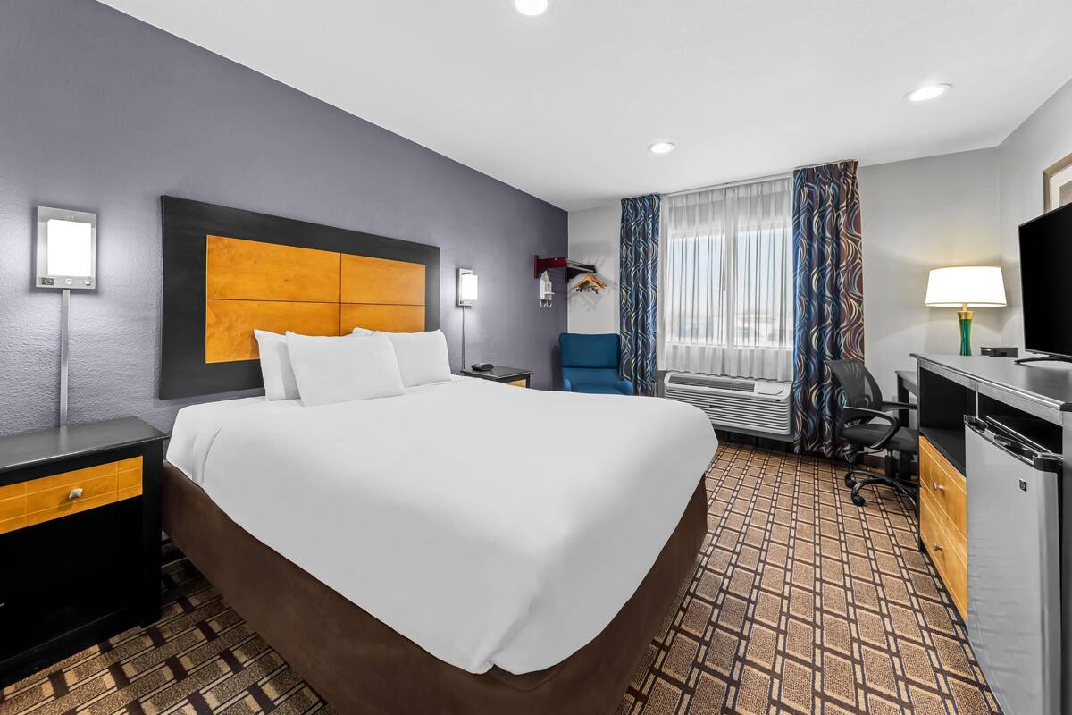 A hotel room with a large bed, a desk with a computer, a chair, and a TV.