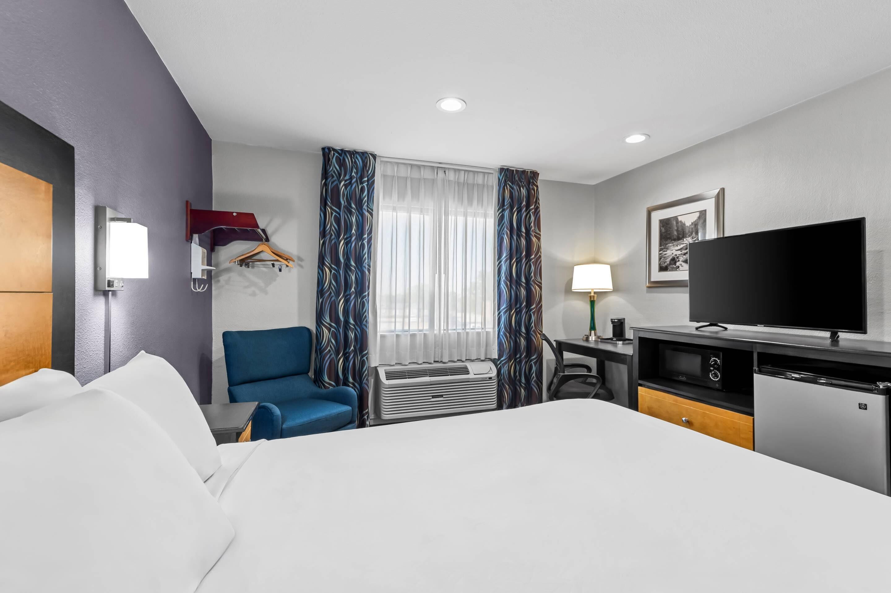 Una habitación de hotel con cama, escritorio, silla, televisor y armario.