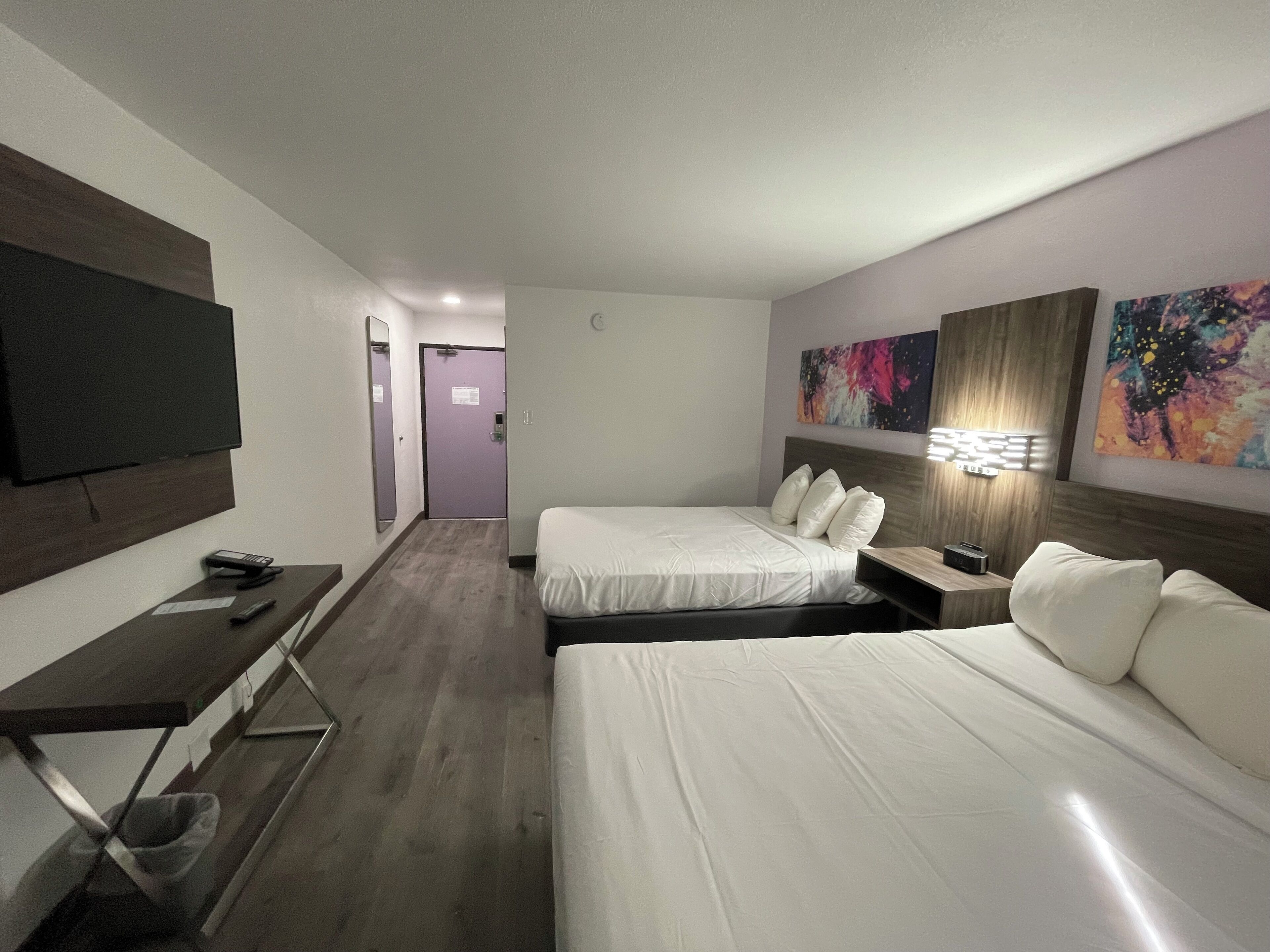 A hotel room with two beds, a TV, a desk, and artwork on the walls.