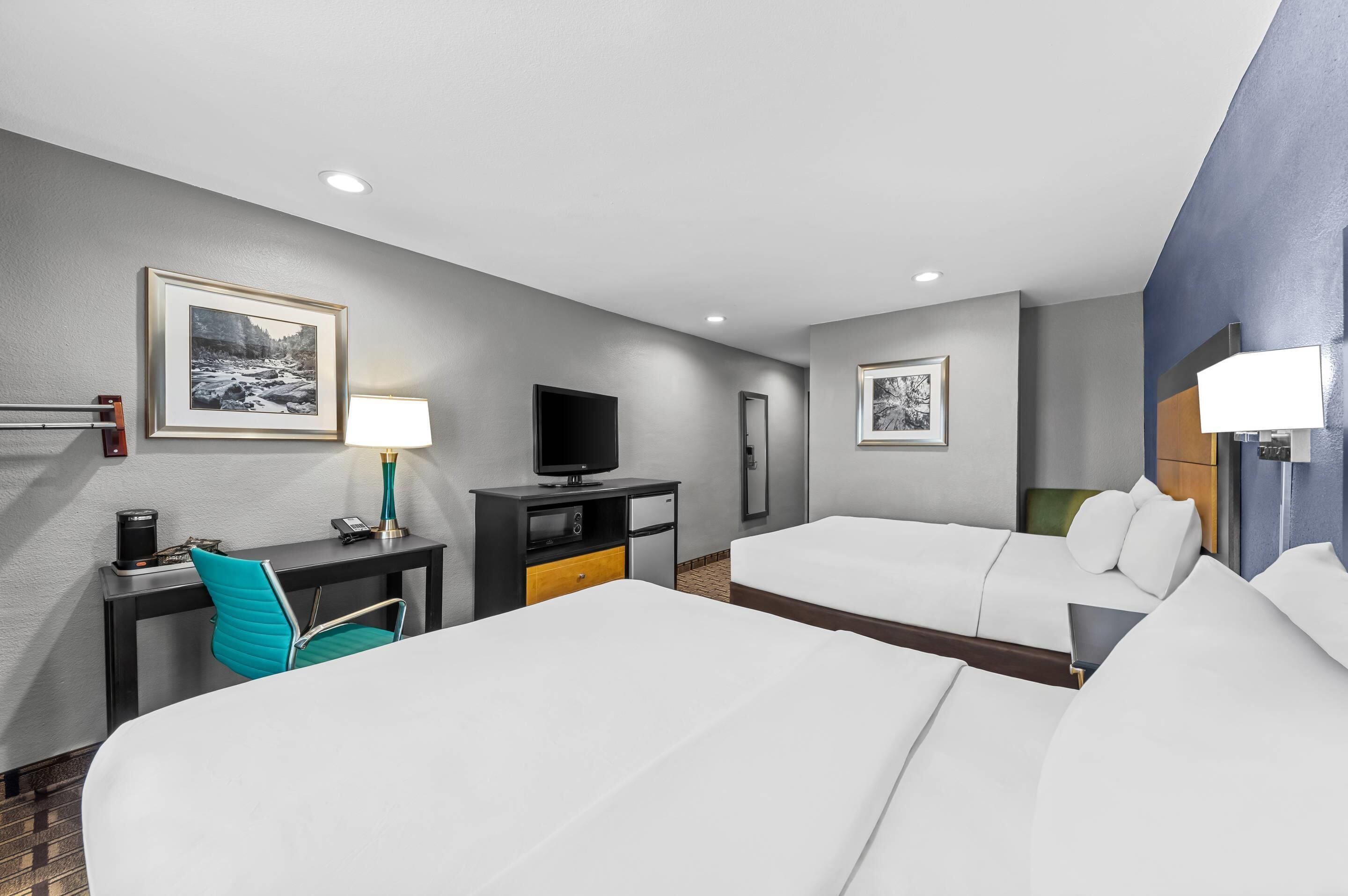 A hotel room with two beds, a desk with a chair, a television, and framed pictures on the walls.