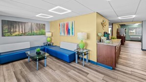 A modern lobby with a blue sofa, glass coffee table, and a painting of a forest.