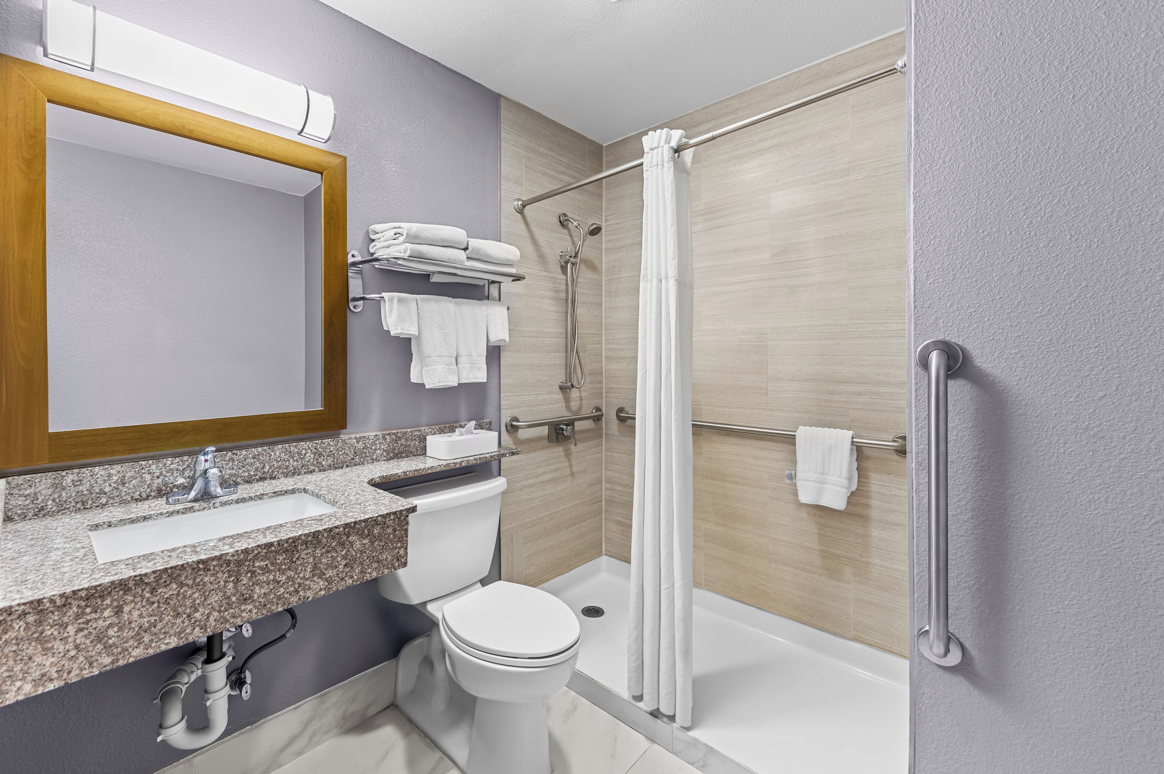 A modern bathroom with a granite countertop, a white toilet, a glass-enclosed shower, and a wooden-framed mirror.
