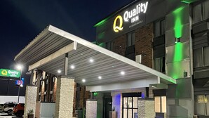 A hotel exterior with a covered entrance, stone pillars, and a sign for 'Quality Inn by Choice Hotels'.