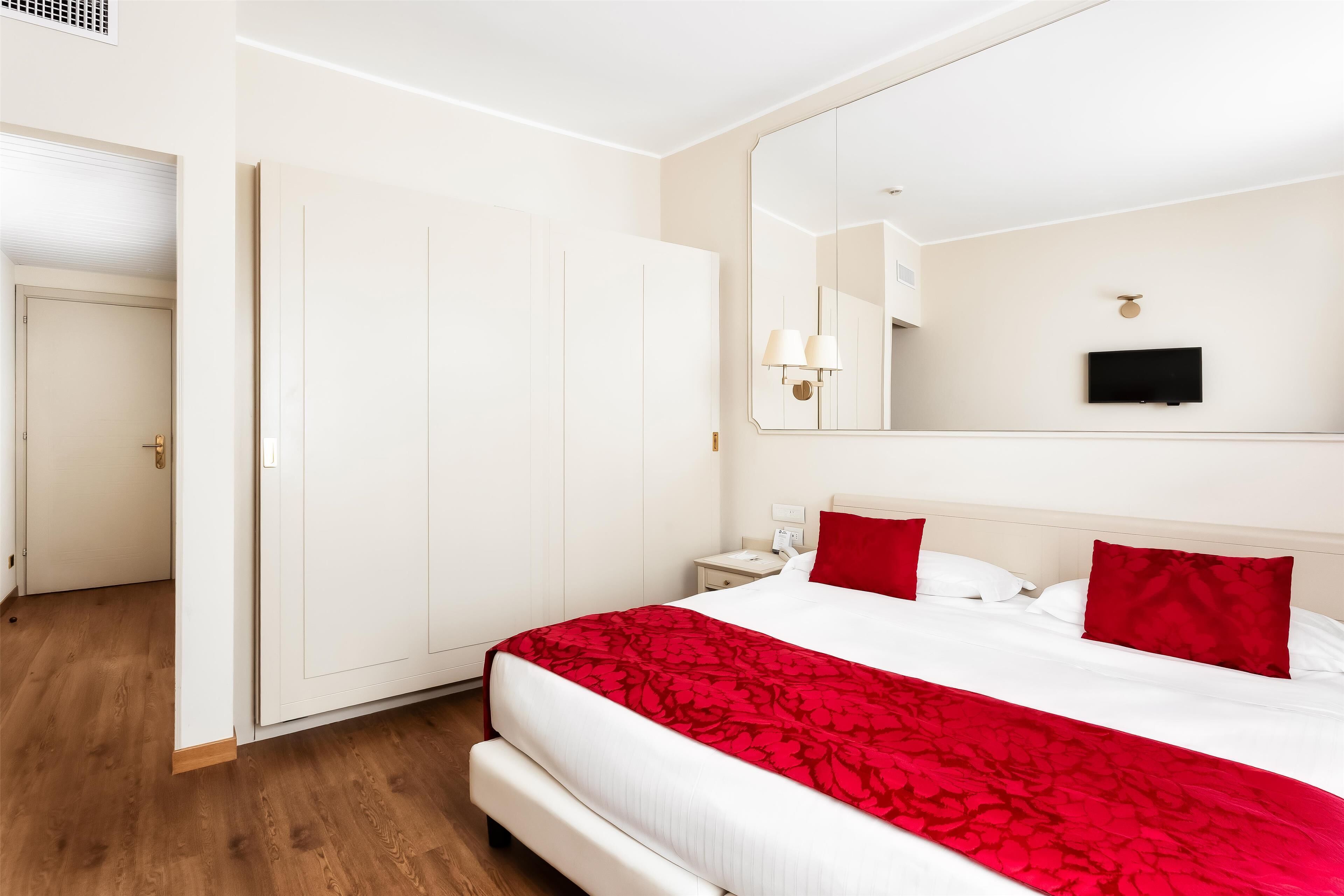 Ein Hotelzimmer mit einem großen Bett, einem Kleiderschrank, einem Nachttisch, einem Spiegel und einem Fernseher.