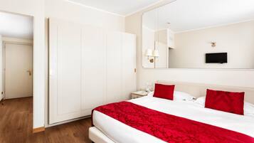 Ein Hotelzimmer mit einem großen Bett, einem Kleiderschrank, einem Nachttisch, einem Spiegel und einem Fernseher.