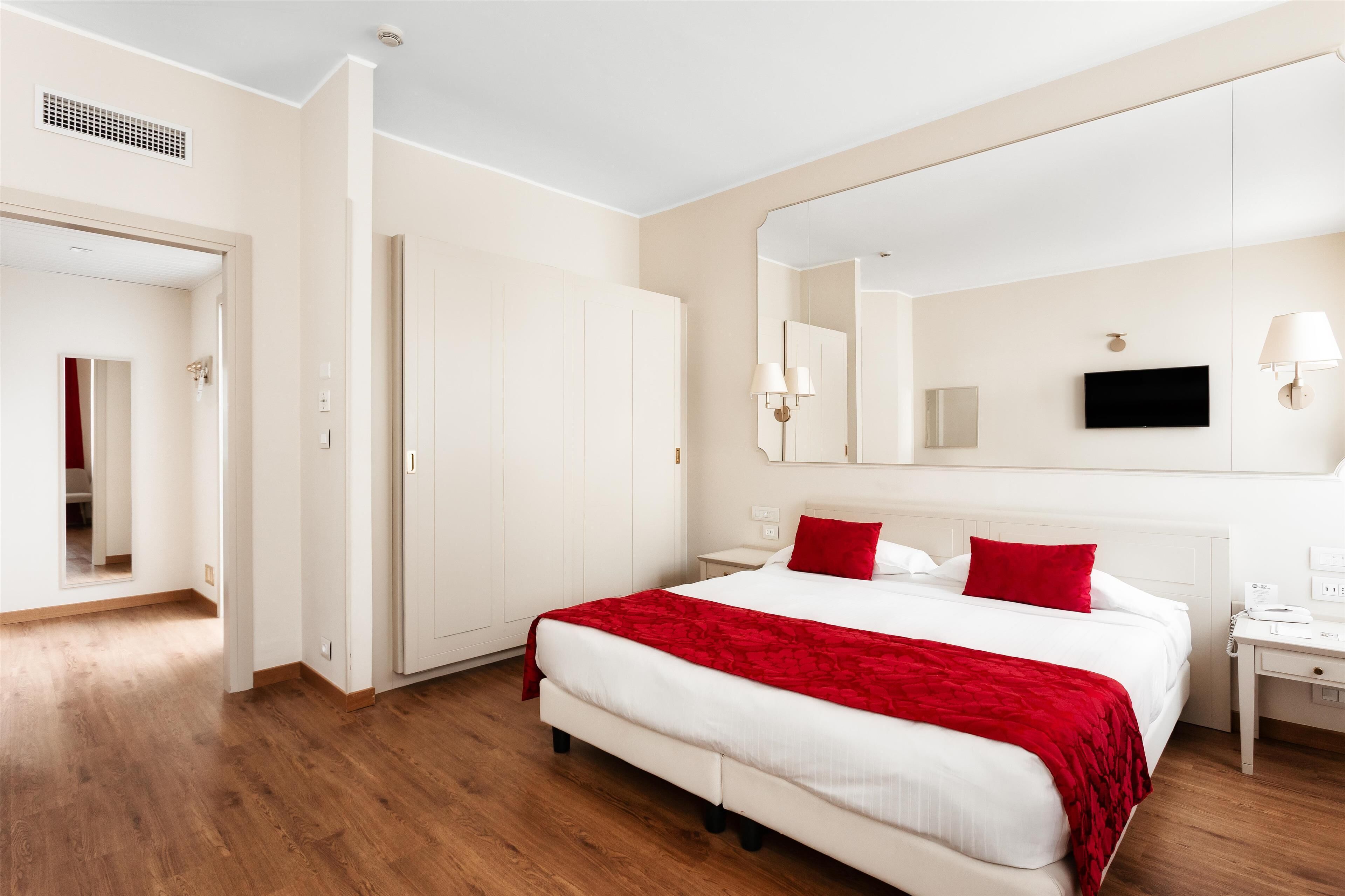 Una habitación de hotel con una cama grande, una mesita de noche, un televisor y un espejo.