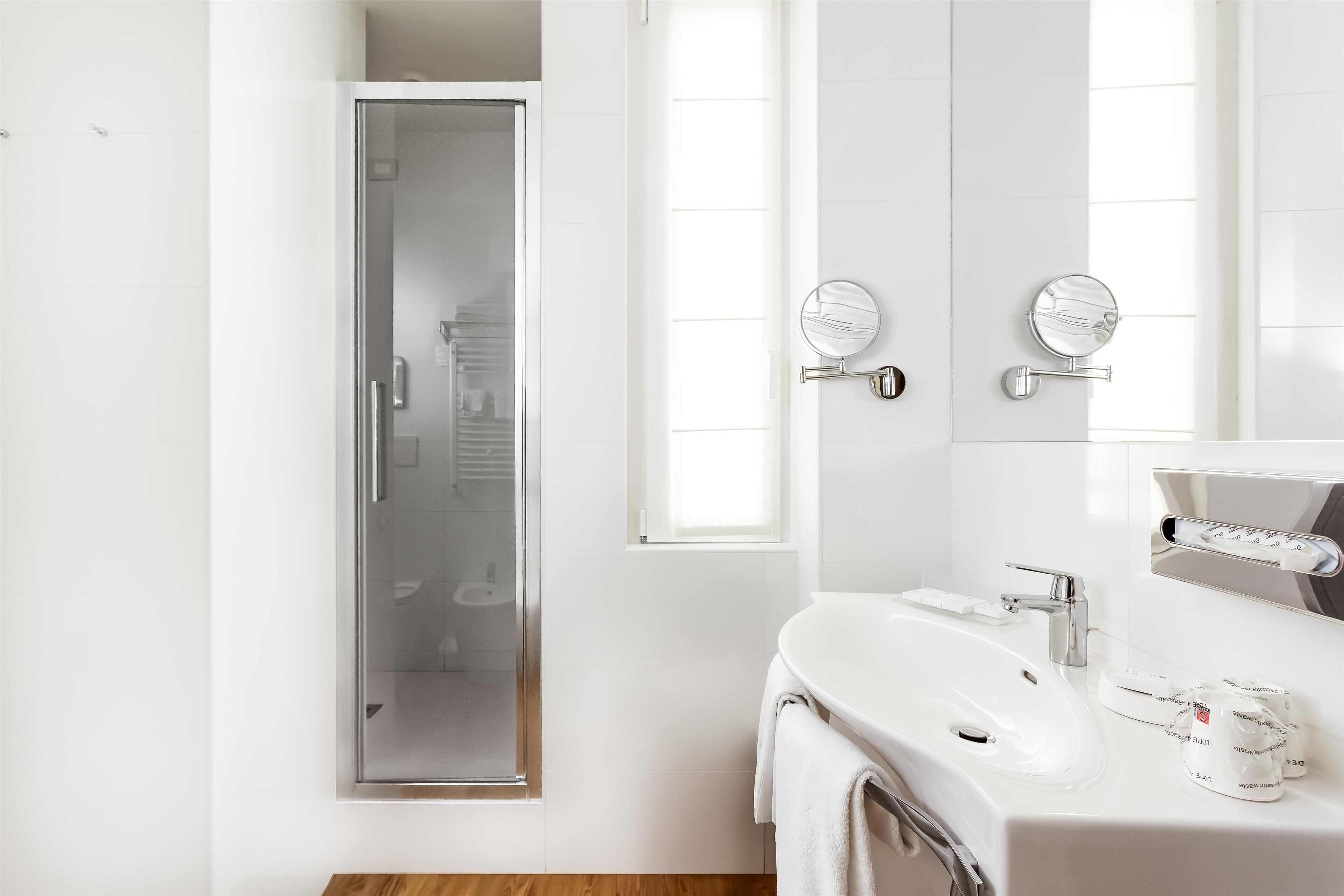 A modern bathroom with a glass shower door, a white sink, and two round mirrors.