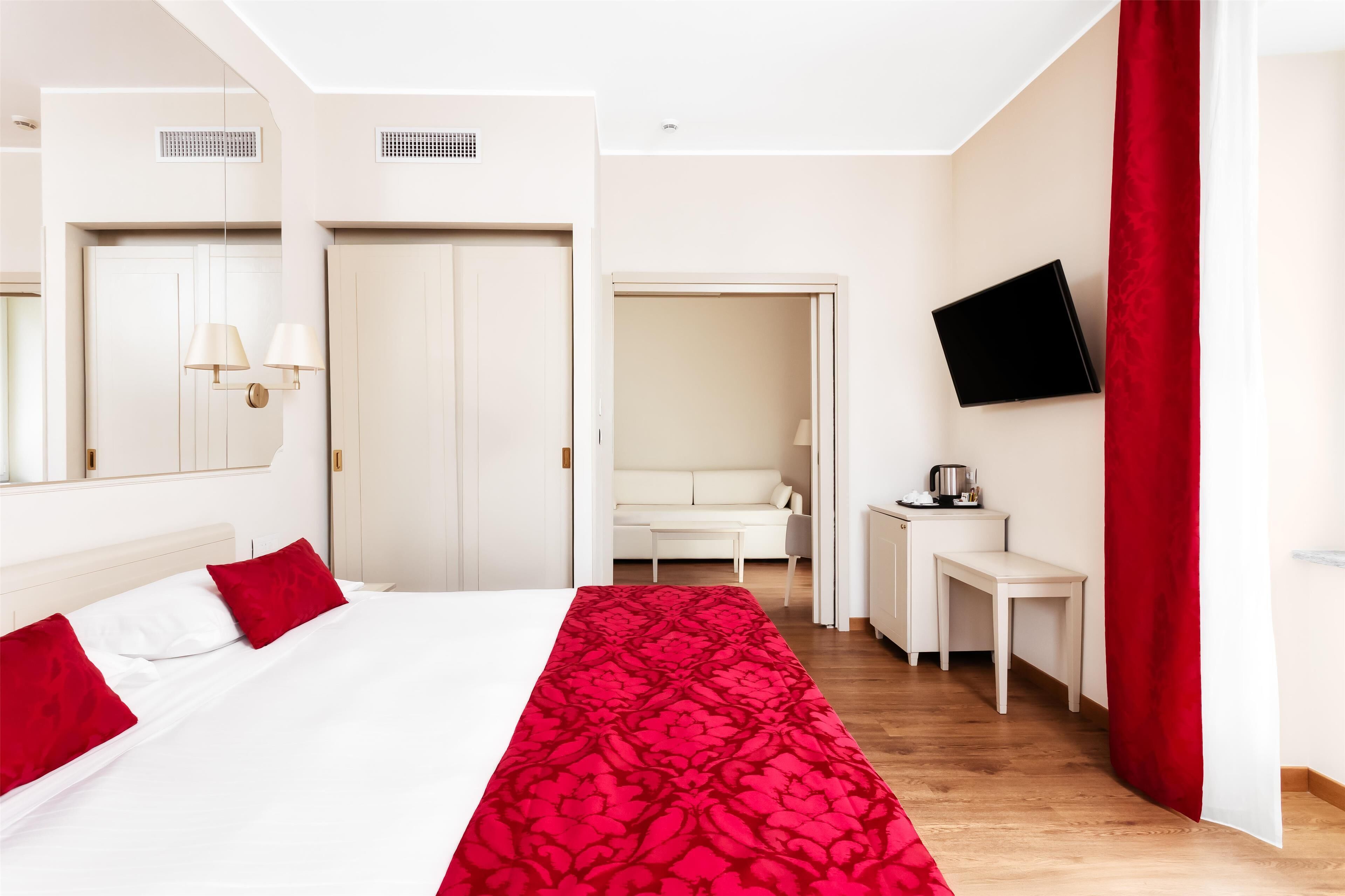 Hotellihuone, jossa on sänky, työpöytä, televisio ja punainen verho.