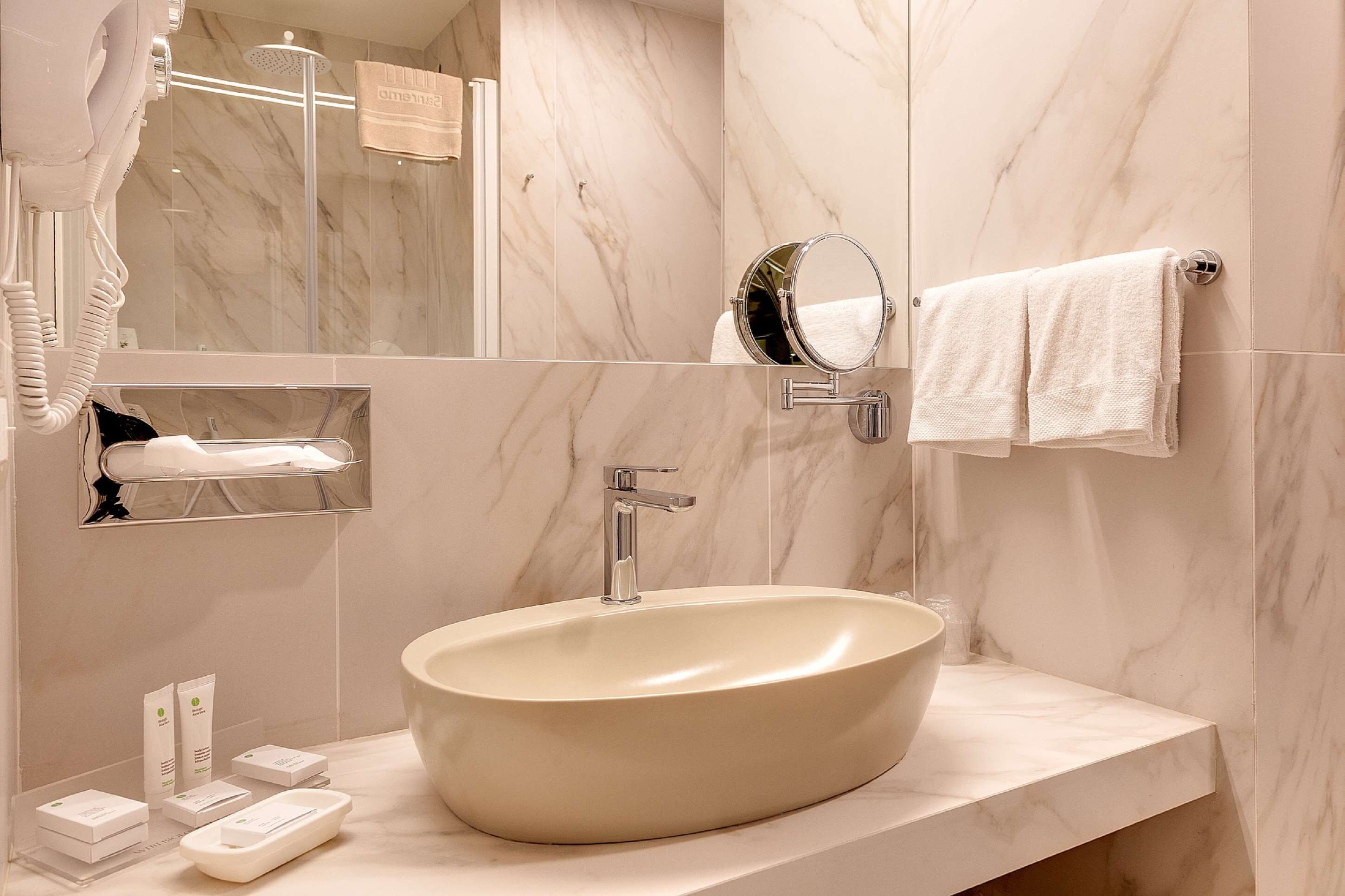 A modern bathroom with a large oval sink, a handheld showerhead, a mirror, and a towel rack.
