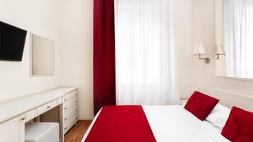 Habitación de hotel con cama, escritorio, silla, televisor y ventana con cortinas.