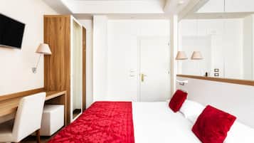 Una habitación de hotel con cama, escritorio, silla, televisor y armario.